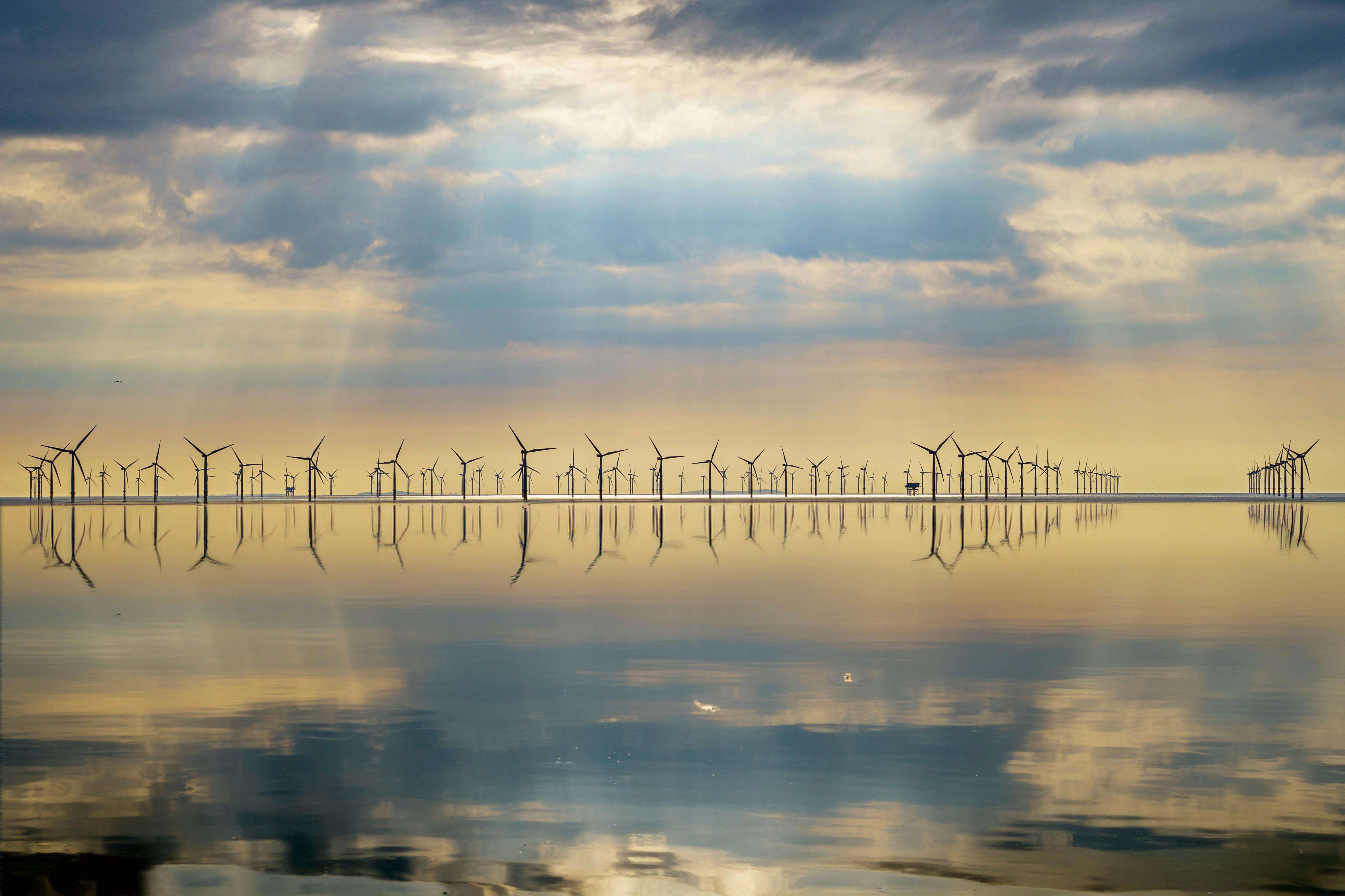 Wind turbines reflected in calm water at an offshore wind farm