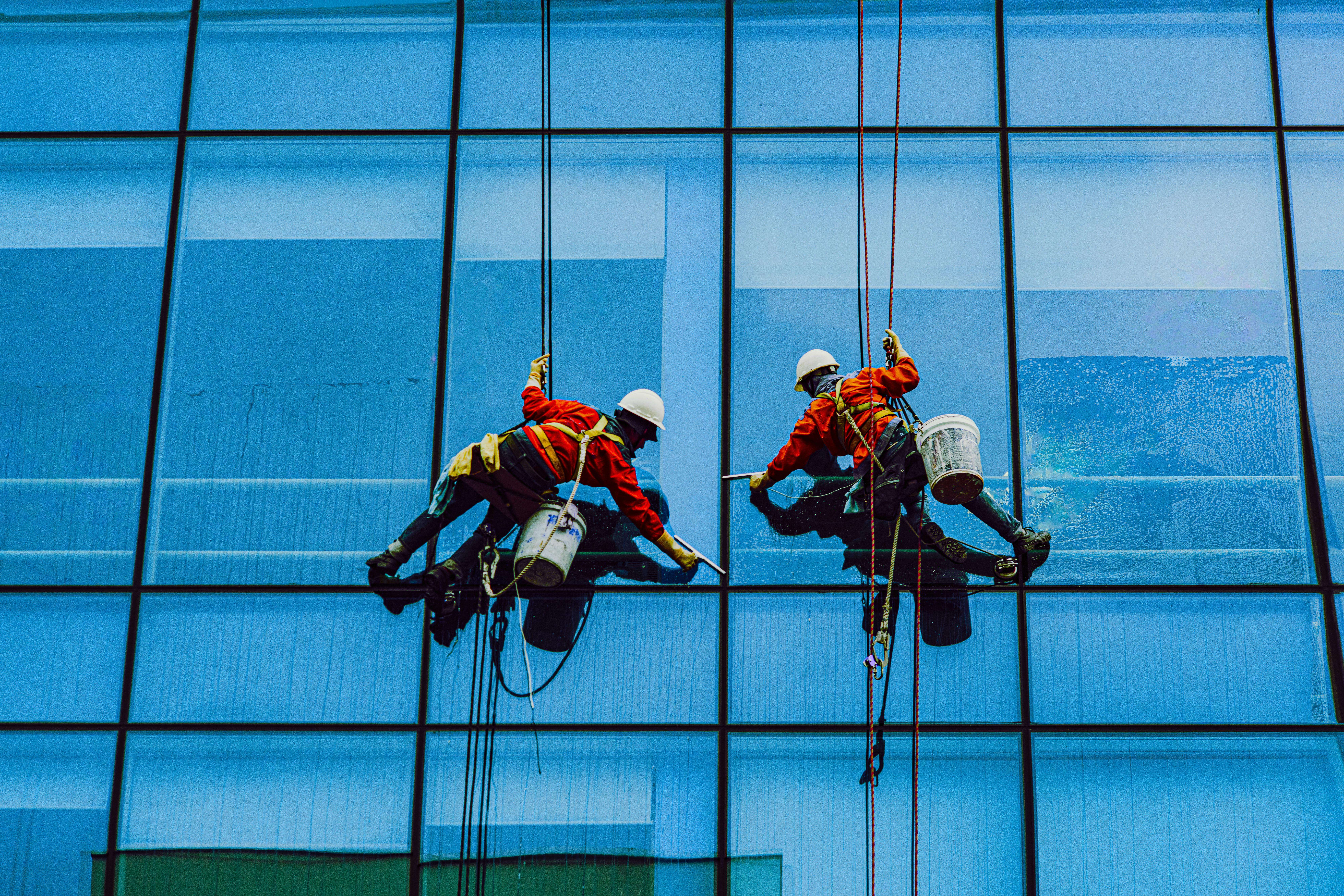 Rope access window cleaners in red safety suits on a glass skyscraper